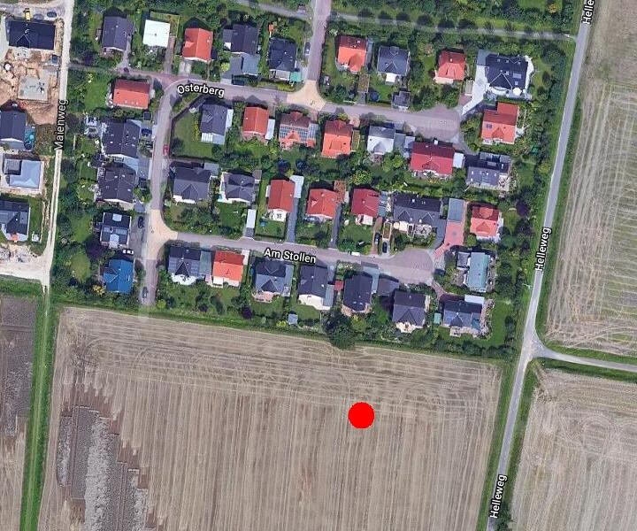 Luftbild einer Wohnsiedlung mit Feldern daneben; roter Punkt markiert unbebautes Grundstück.