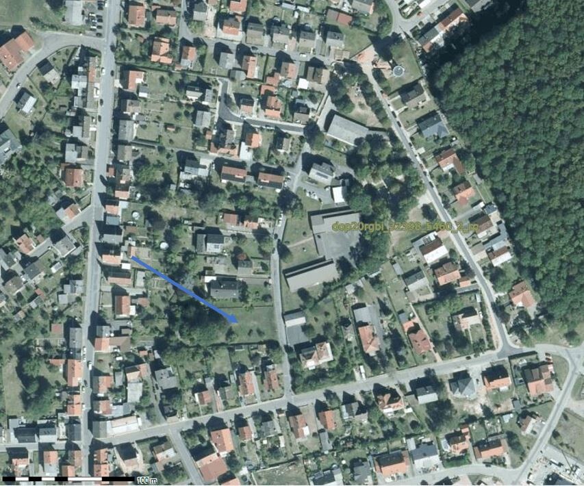 Luftbild eines Wohnviertels mit Häusern, Straßen, Gärten, Wald am rechten Rand.
