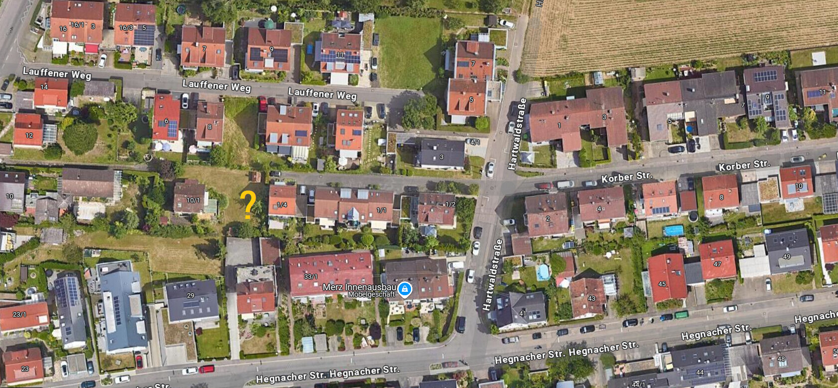 Satellitenbild einer Wohnsiedlung mit Straßen; gelbes Fragezeichen markiert ein Grundstück.