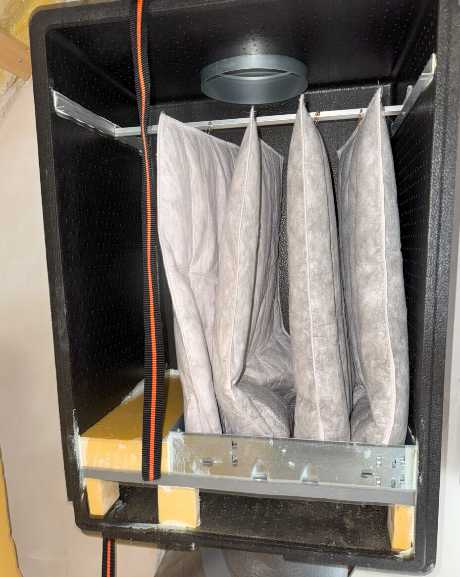 Innenansicht eines schwarzen Safes mit grauen Stofffächern, die an einem Metallgestell hängen.