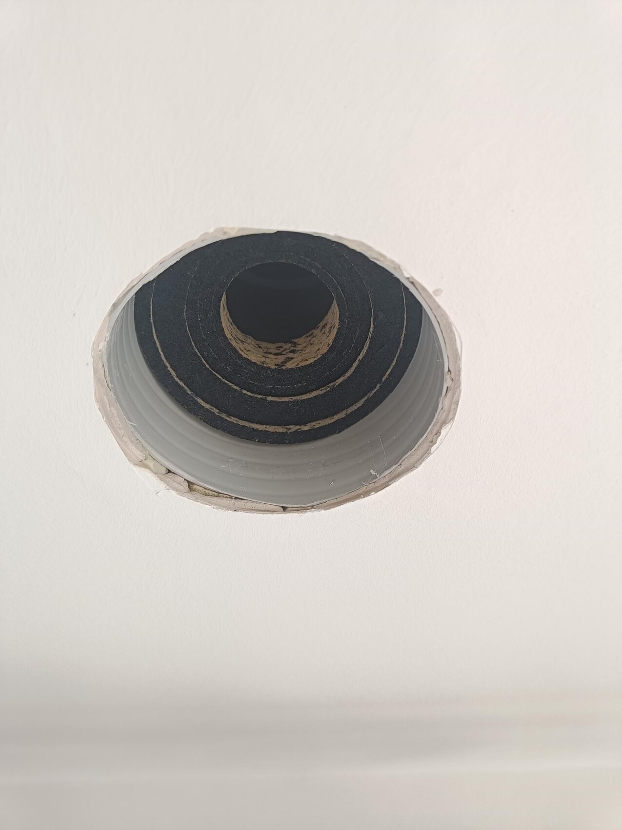 Runder Lüftungsschacht in der Decke mit schwarzer Dämmung sichtbar