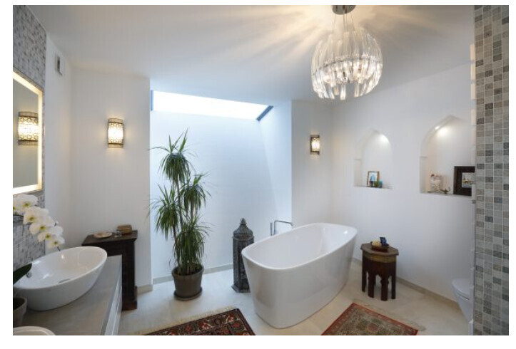 Geräumiges Bad mit freistehender weißer Badewanne, Pflanze, Kronleuchter und Mosaikwand.