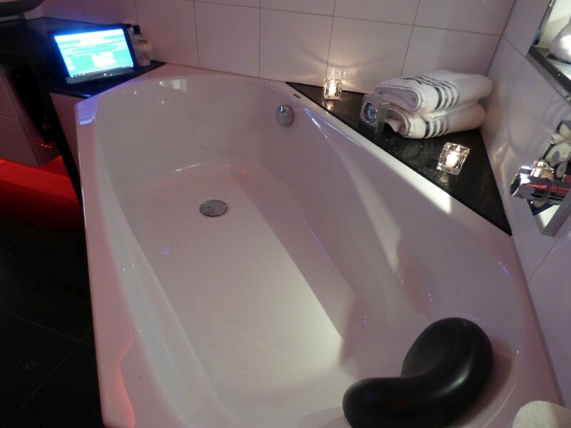 Moderne Badewanne im Badezimmer, Kerzen, zwei Handtücher und Laptop am Rand.