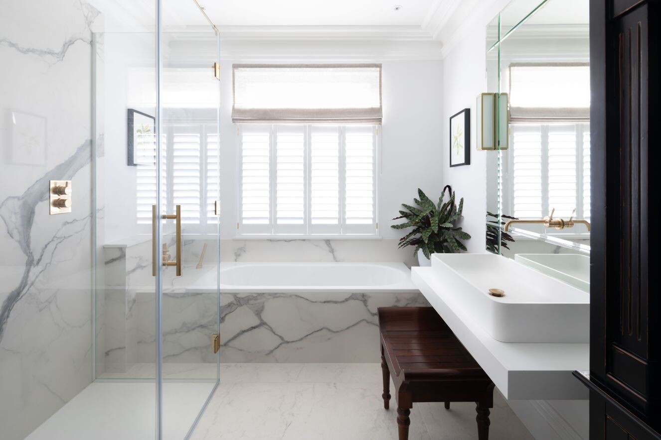 Weißes Marmorbadezimmer mit Glasdusche, Badewanne, Waschbecken, Fensterläden, Pflanze