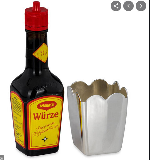 Maggi Würze Flasche mit rotem Deckel neben einem silbernen Metallbehälter.