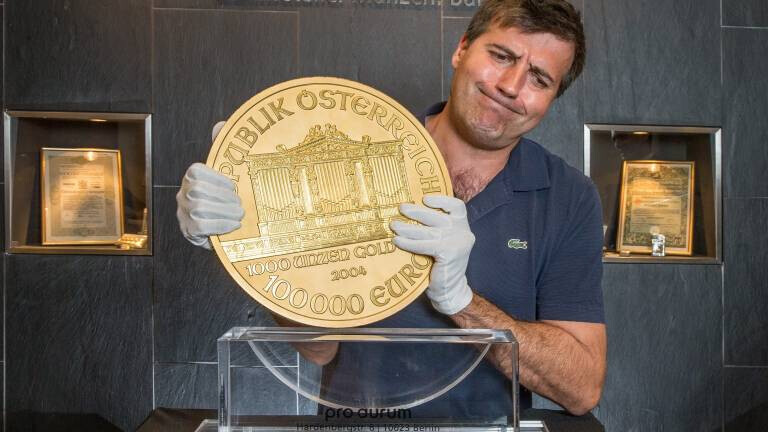 Ein Mann mit weißen Handschuhen präsentiert eine riesige Goldmünze vor einer Glasvitrine.