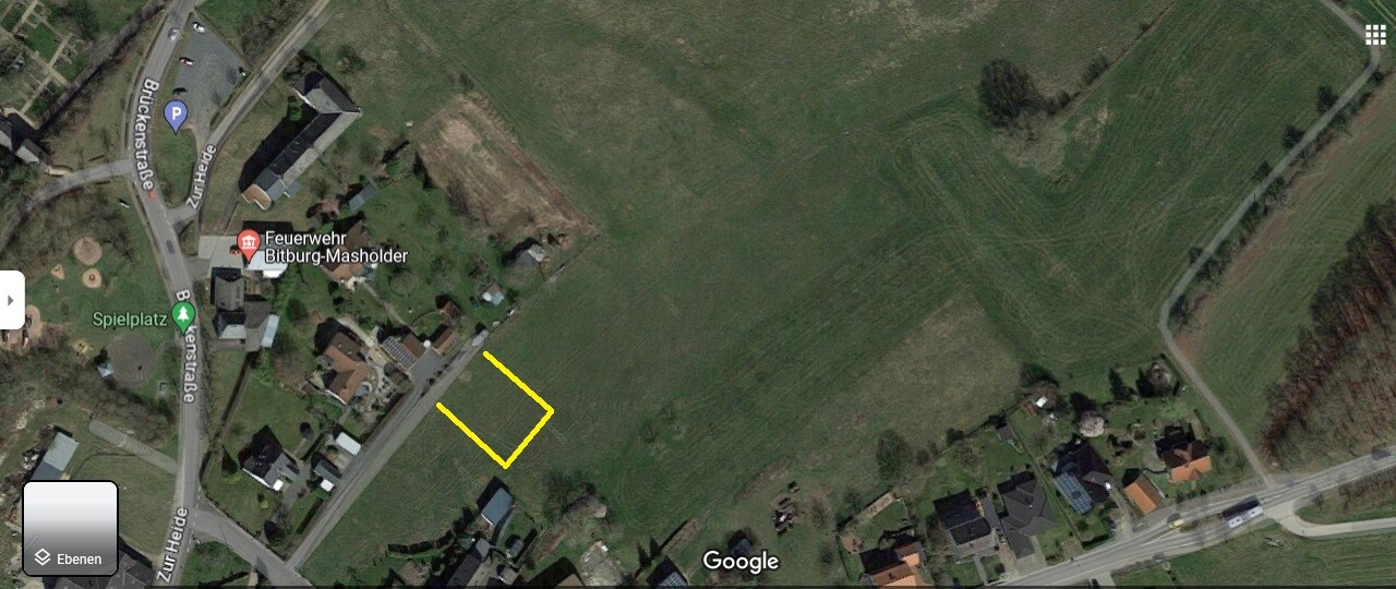Satellitenbild: Gelb markierte L-förmige Fläche neben Häusern an einer Straße.