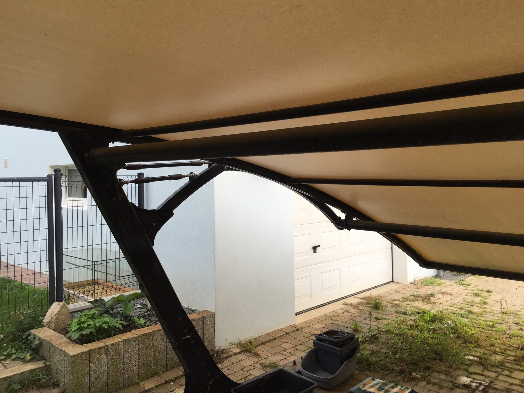 Unterseite eines ausklappbaren Terrassendachs mit beigem Stoff und schwarzem Metallrahmen.
