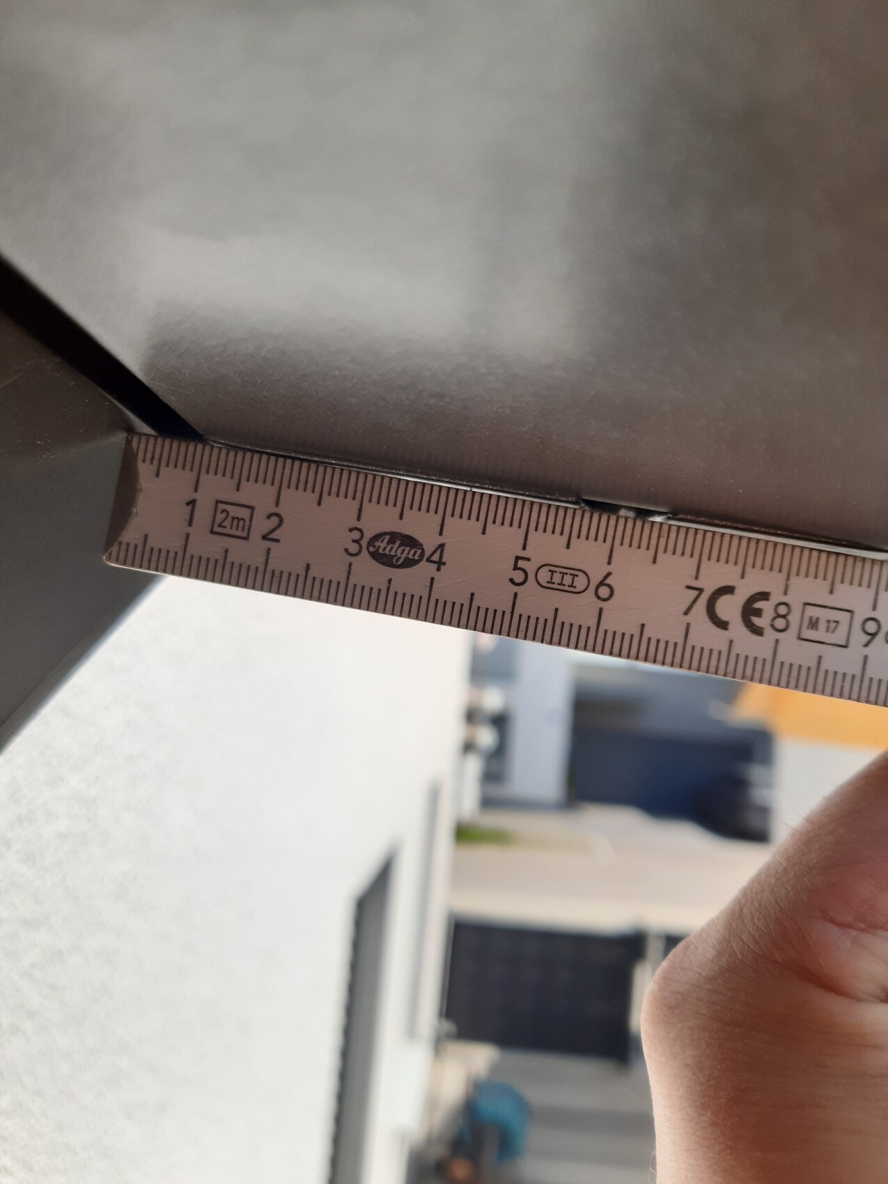 Nahaufnahme eines Maßbands über einer Metallkante; zeigt ca. 3,5 cm, rechte Hand im Bild.