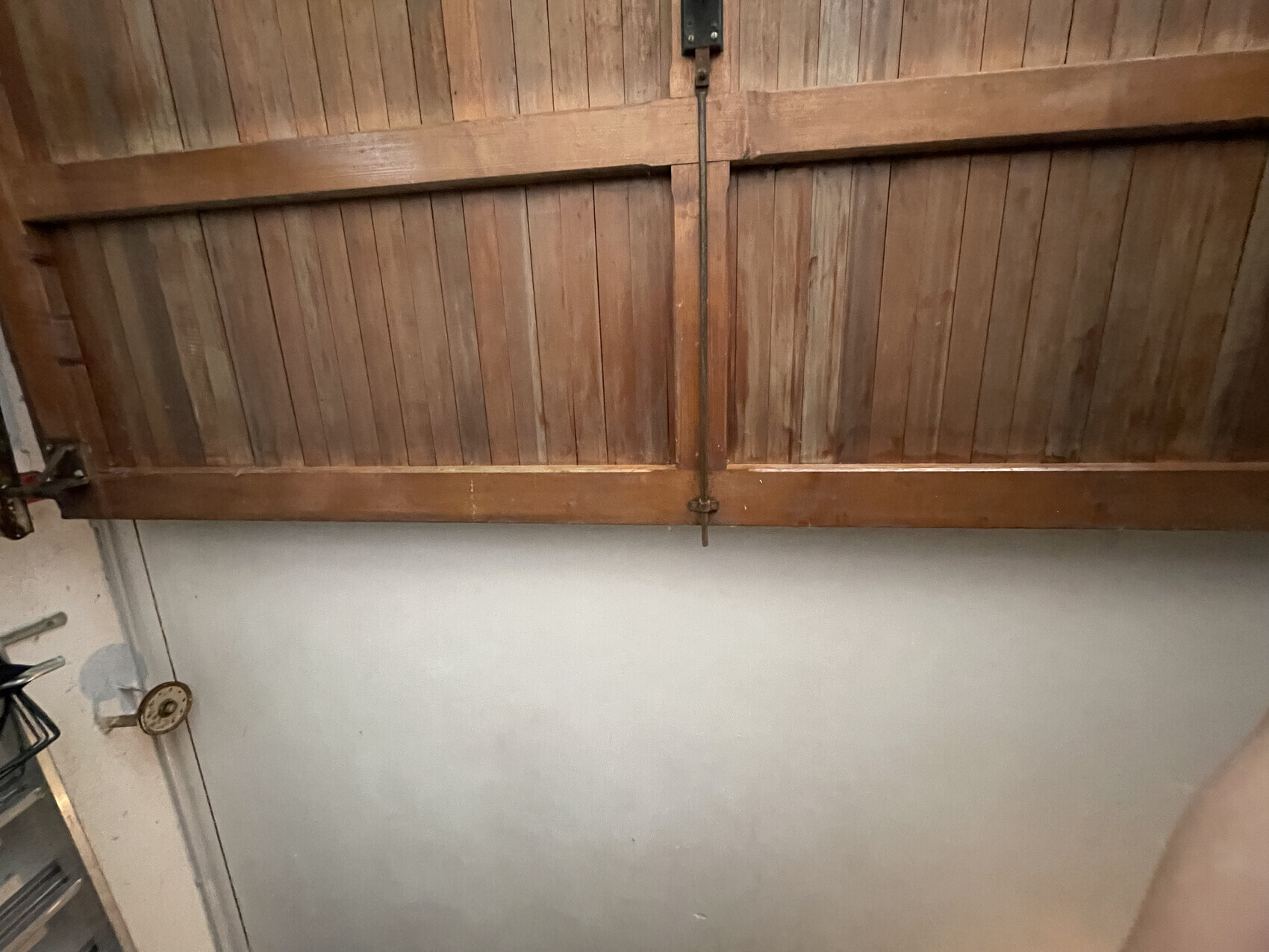 Holzlatten-Tor mit senkrechten Brettern und zentralem Metallriegel, darunter Betonwand.
