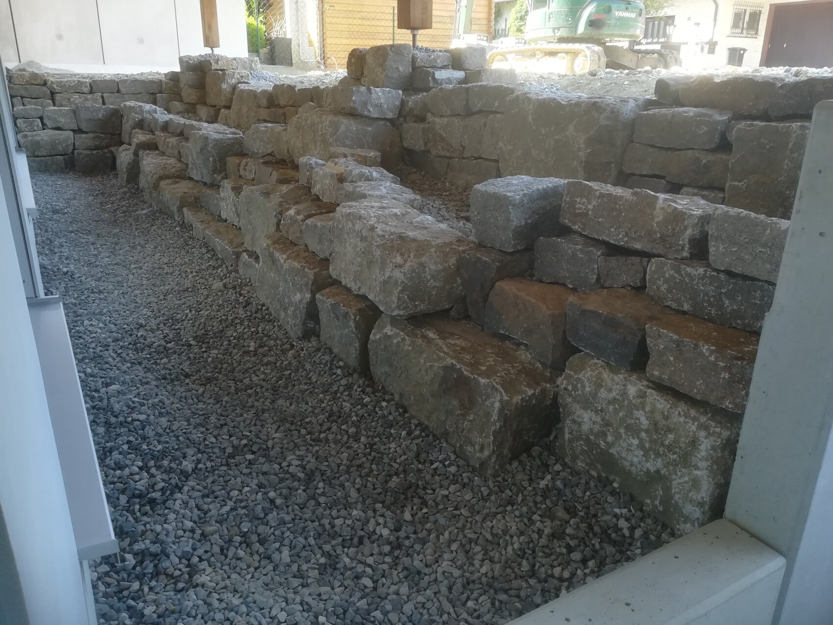Massive Steinmauer wird auf einer Baustelle aufgebaut, Kiesboden davor.