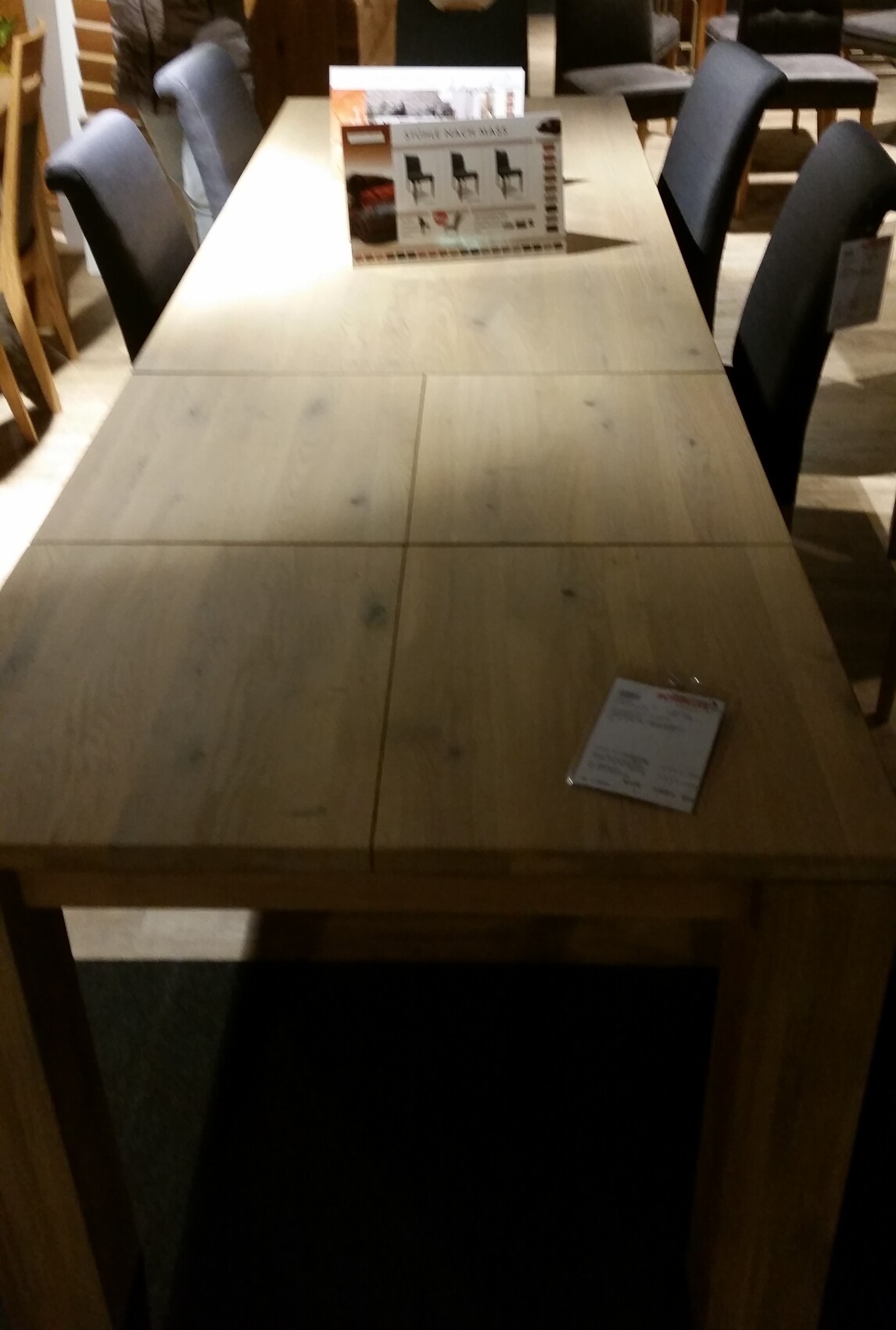 Langer Holztisch mit Stühlen in Möbelhaus; Werbeprospekt in der Mitte