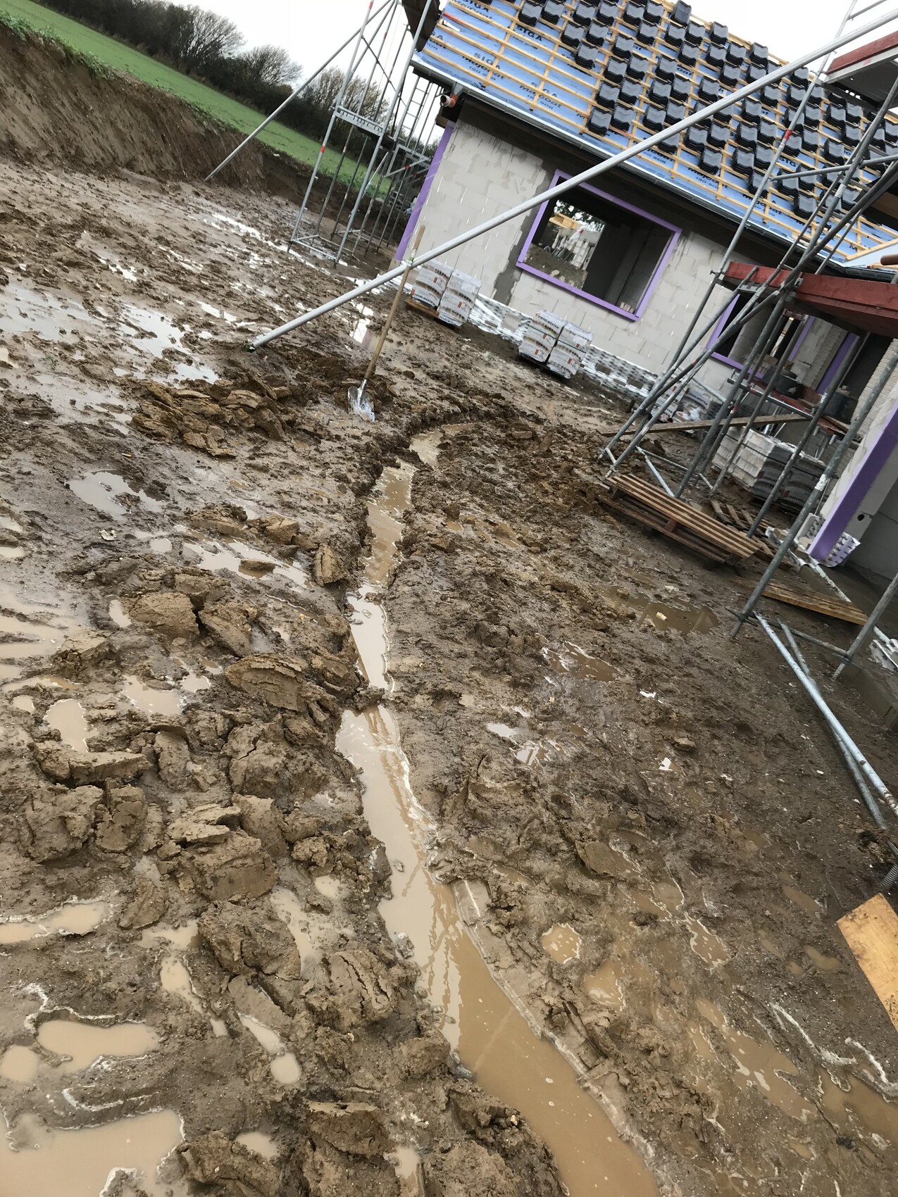 Matschige Baustelle mit unfertigem Rohbau, Gerüsten, Baustoffen