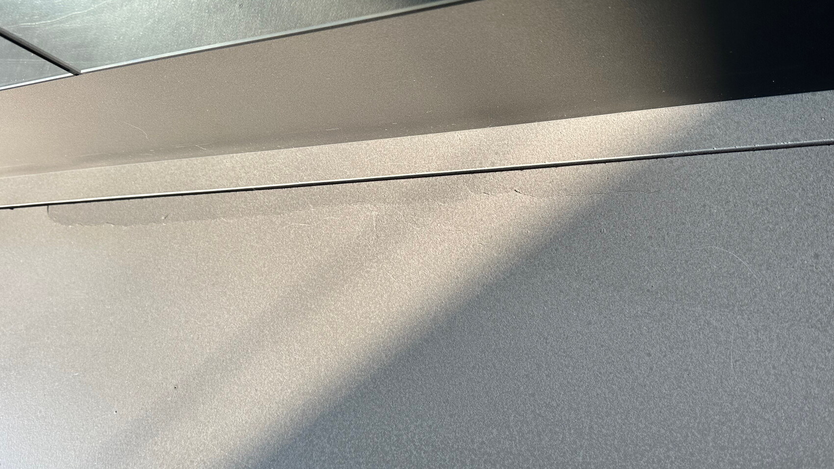 Nahaufnahme einer staubigen Fahrzeugoberfläche mit Kratzern und einer Naht zwischen Blechen.