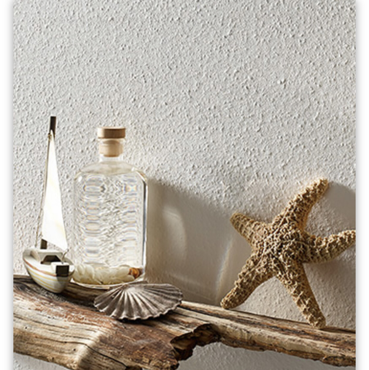 Strand-Dekor mit Flasche und Korken, Segelboot, Muscheln und Seestern auf Treibholz