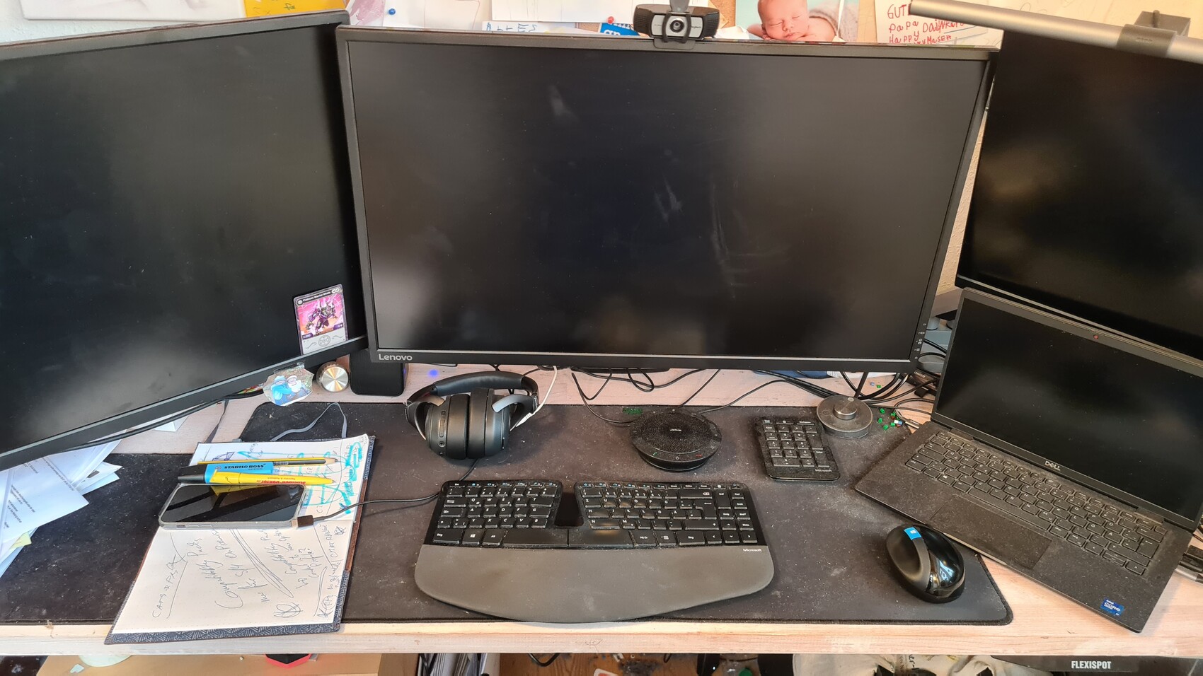Arbeitsplatz mit drei Monitoren, Laptop rechts, Headset, Tastatur, Maus; Webcam oben.