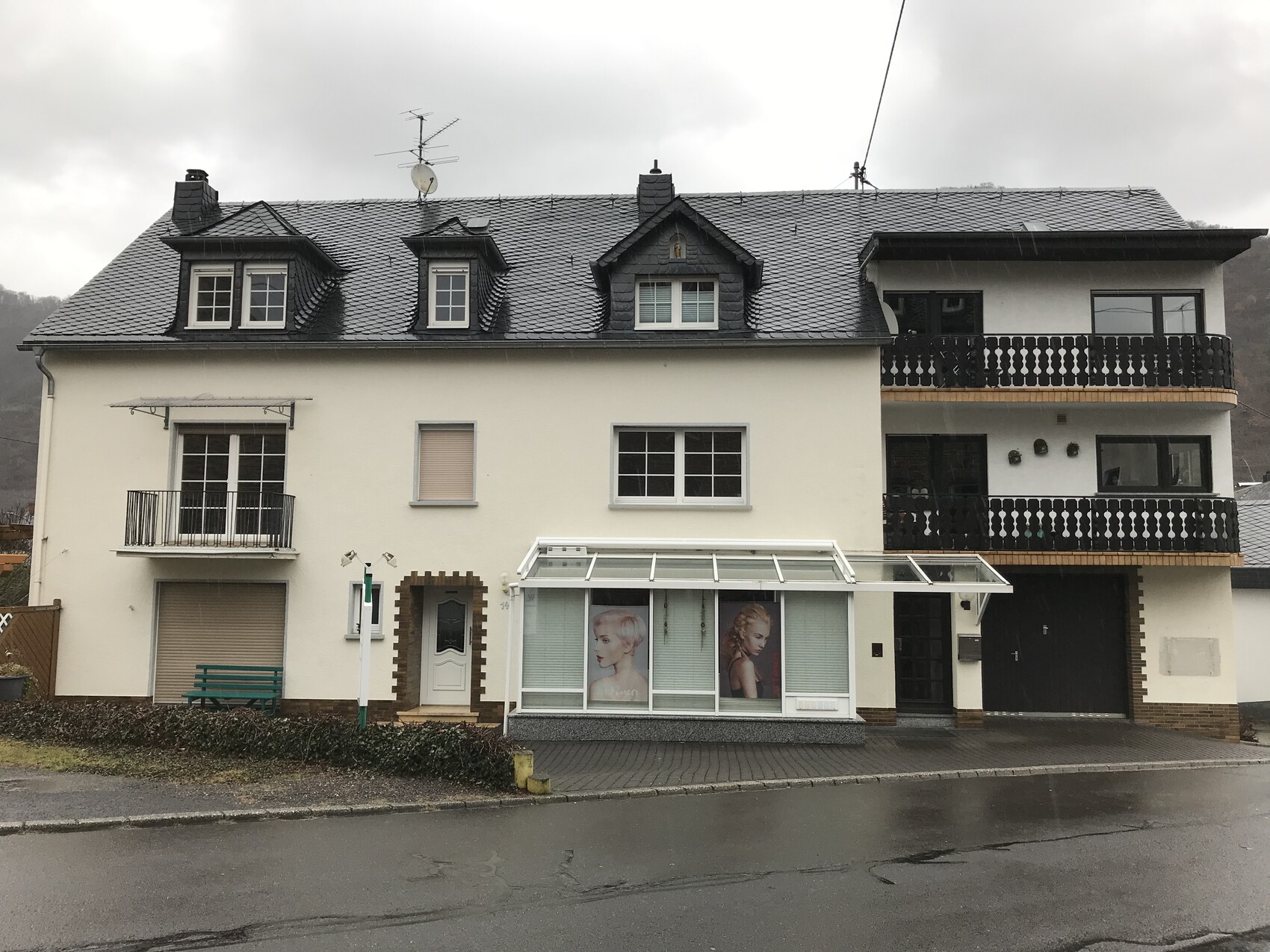 Mehrfamilienhaus mit Dachgauben, Balkonen und Glasvordach.