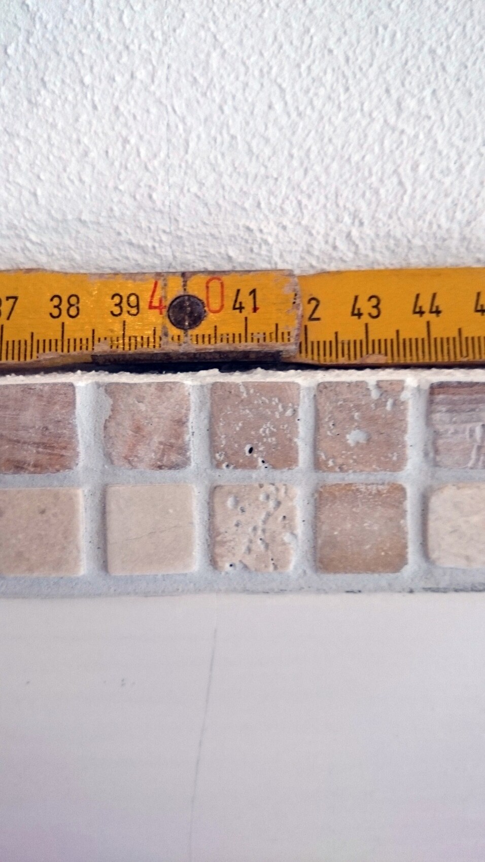Messband liegt über beige Bodenfliesen an einer Wand im Bad