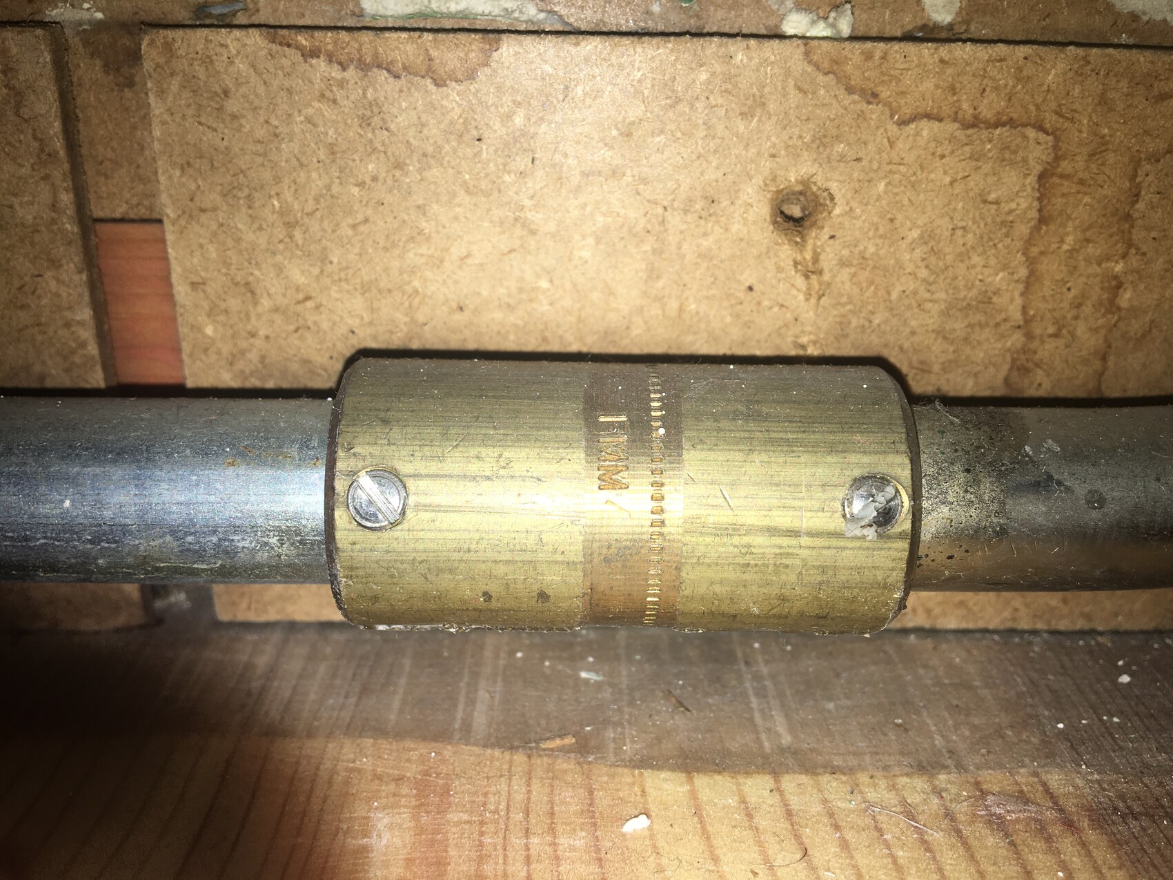 Messing-Schelle um ein Metallrohr mit zwei Schrauben, auf Holzuntergrund.