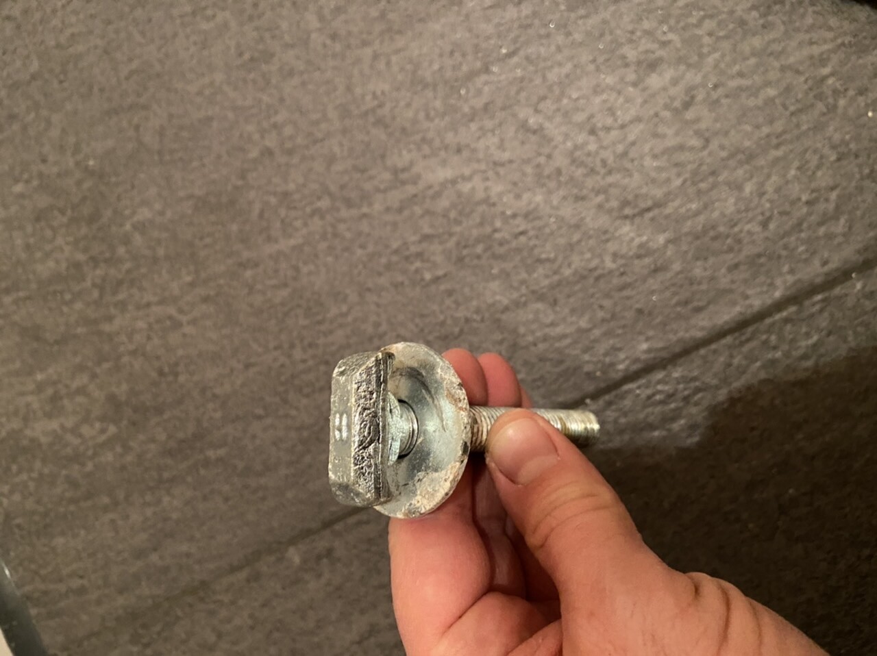 Nahaufnahme eines Metallbolzens mit Gewinde und rundem Kopf, in einer Hand gehalten.
