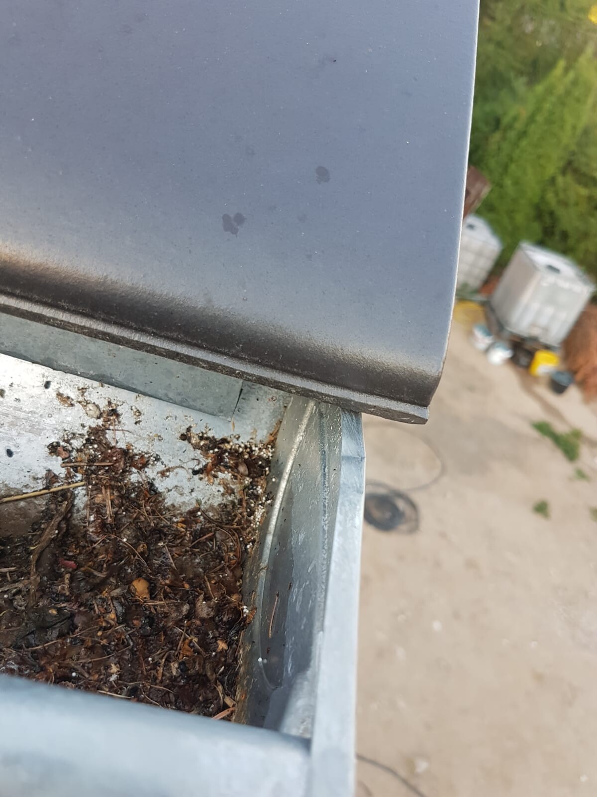Nahaufnahme einer metallischen Dachrinne mit Laub und Schmutz, Baustellenumgebung im Hintergrund