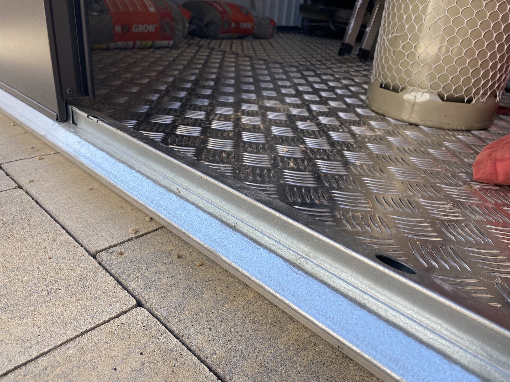 Offene Fahrzeugtür mit Diamantplattenboden, blauer Rand und Säcke im Hintergrund.