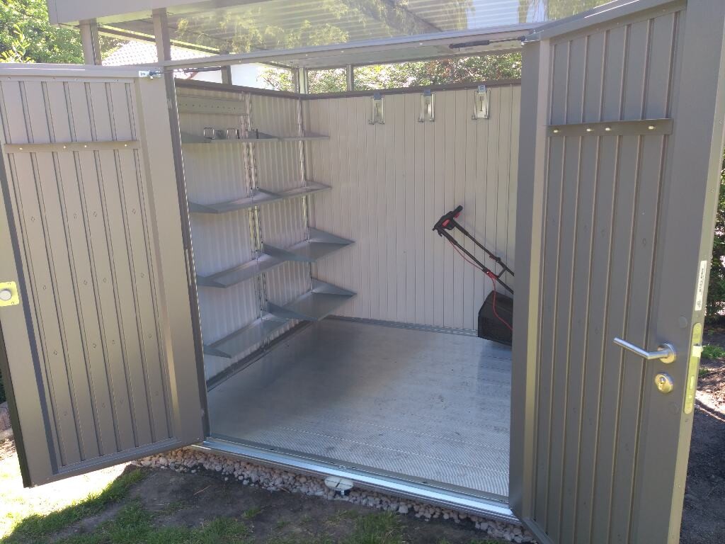 Offener Metall-Lager-Schuppen; linke Wand mit sechs Regalen, Rasenmäher hinten rechts.