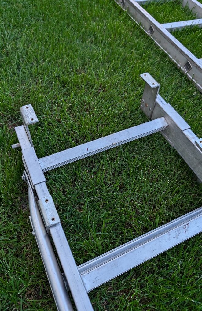 Zerlegtes verzinktes Metallgestell liegt zerlegt auf Gras; vermutlich Gerüstteile.