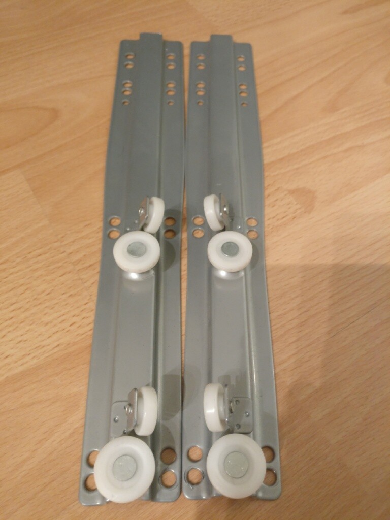 Zwei lange graue Schubladenschienen mit weißen Kunststoffrollen auf Holzboden.