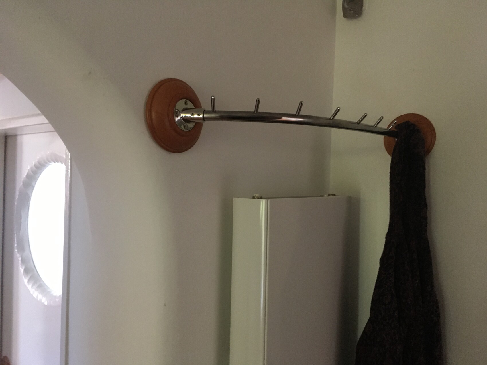 Garderobenstange mit Haken an runden Holzplatten befestigt; dunkler Schal hängt daran.