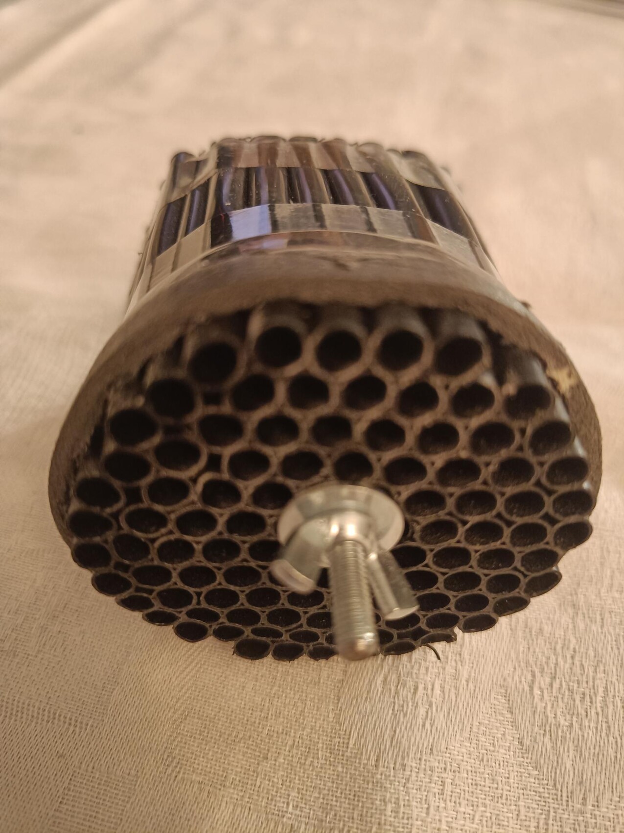 Zylindrischer Metallfilter mit vielen runden Löchern in Honigwabenstruktur; zentrale Schraube sichtbar.