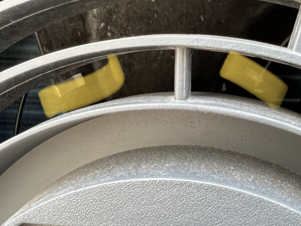 Nahaufnahme eines runden silbernen Metallteils mit Struktur; gelbe Akzente im Hintergrund.
