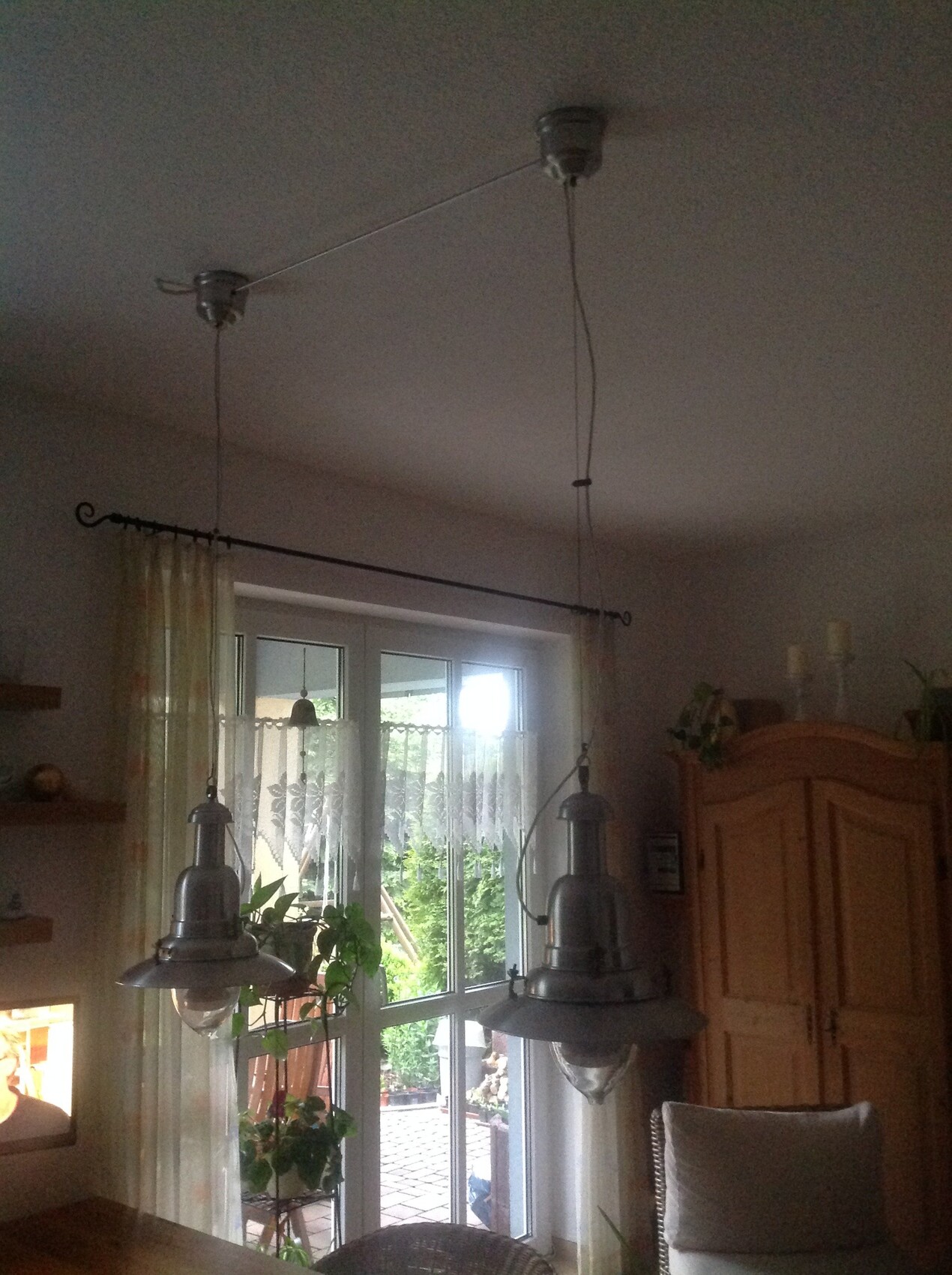 Zwei metallische Hängeleuchten hängen über dem Esstisch in der Küche neben einem Fenster.
