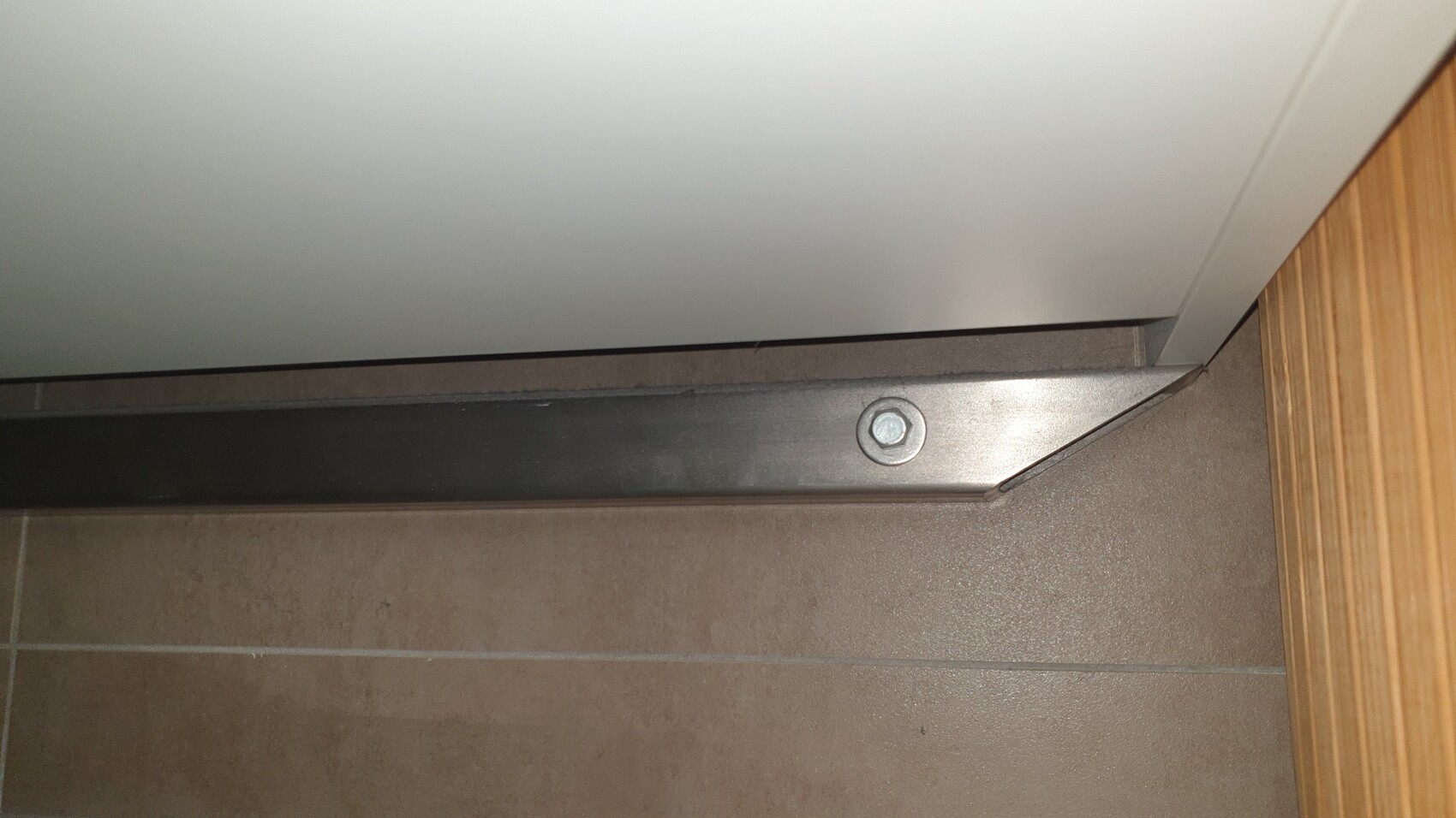 Metall-Tuerenschwelle mit Schraubenkopf, Bodenfliesen, Holzrahmen.