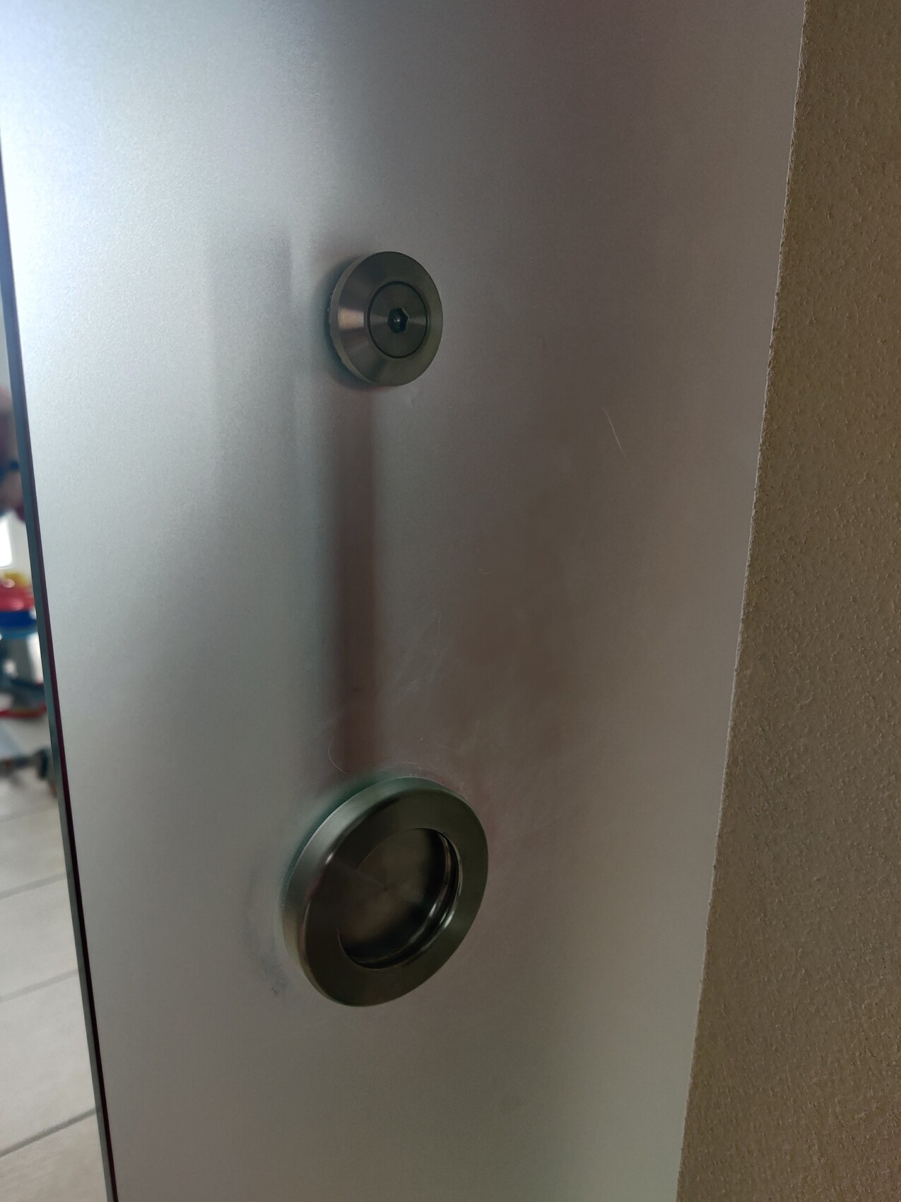 Metallene Türplatte mit zwei runden Beschlägen: oberer Zylinder, unterer Türspion.