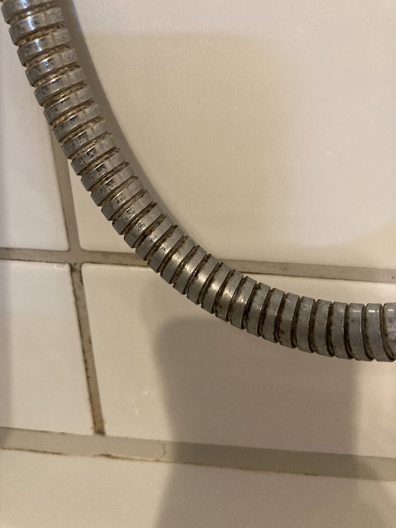Spiralförmiger Metallflexschlauch liegt diagonal über weißen Fliesen.