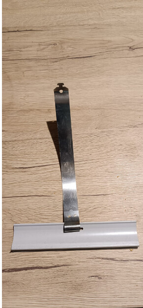 Kleine Metallhalterung mit weißem Kunststofffuß liegt auf Holzboden.