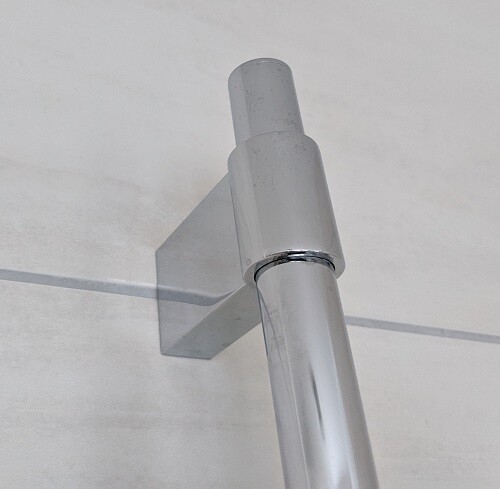 Nahaufnahme eines Chromstahlrohrs mit Wandhalterung an heller Wand.