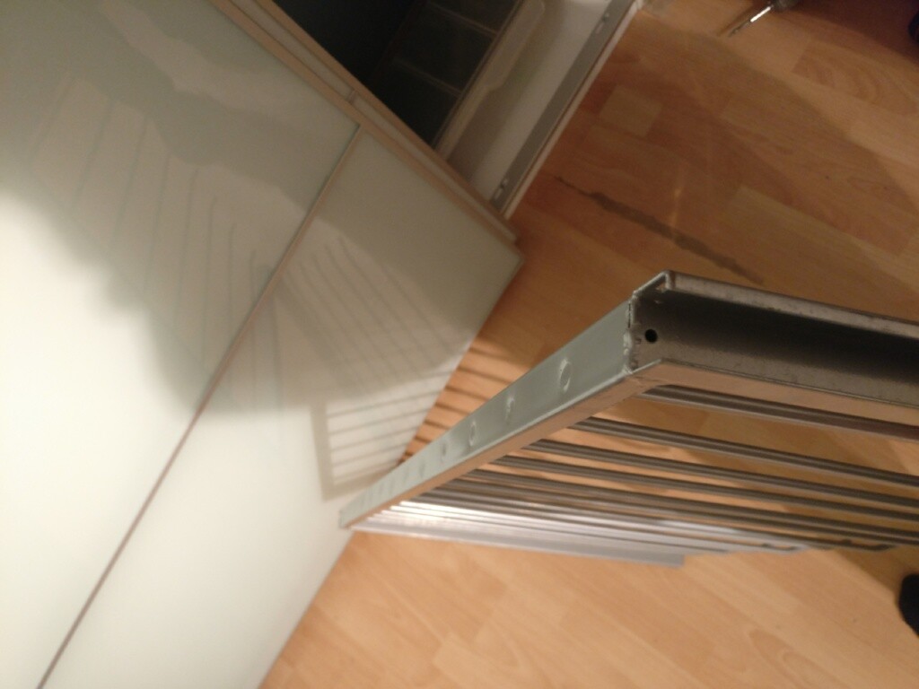 Metallrahmen mit Schraubenlöchern liegt auf Holzboden neben einer Glasvitrine.