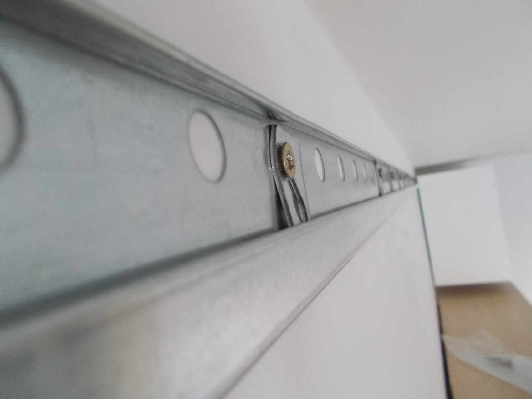 Nahaufnahme einer metallischen Führungsschiene mit Schraube entlang einer Wand