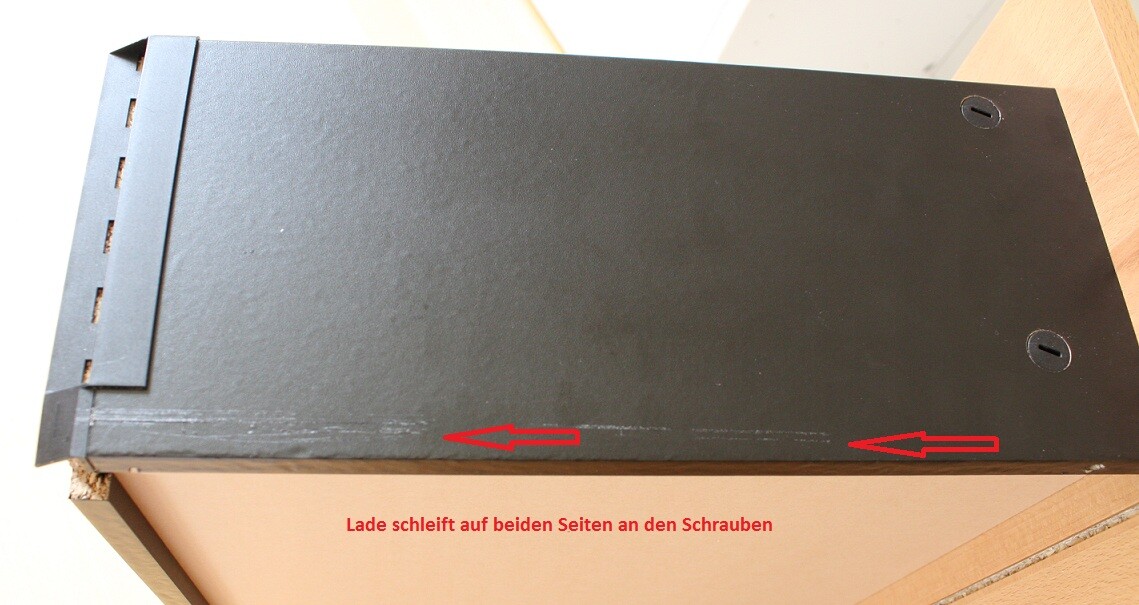 Schwarzes Metallgehäuse auf Unterlage; Unterkante schleift an Schrauben, Pfeile zeigen Kontakt.