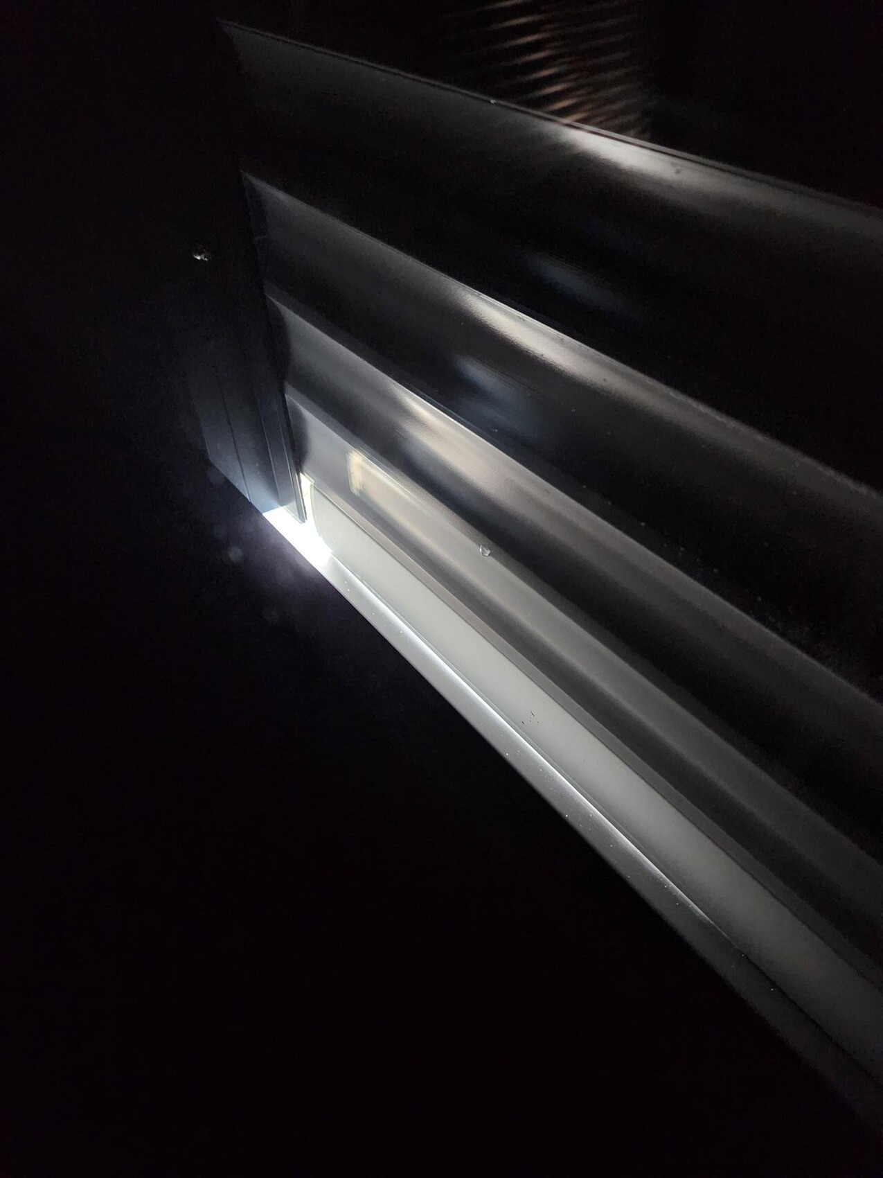 Nächtliche Nahaufnahme einer glänzenden Metall-Schiene mit hellem Licht durch einen Spalt.