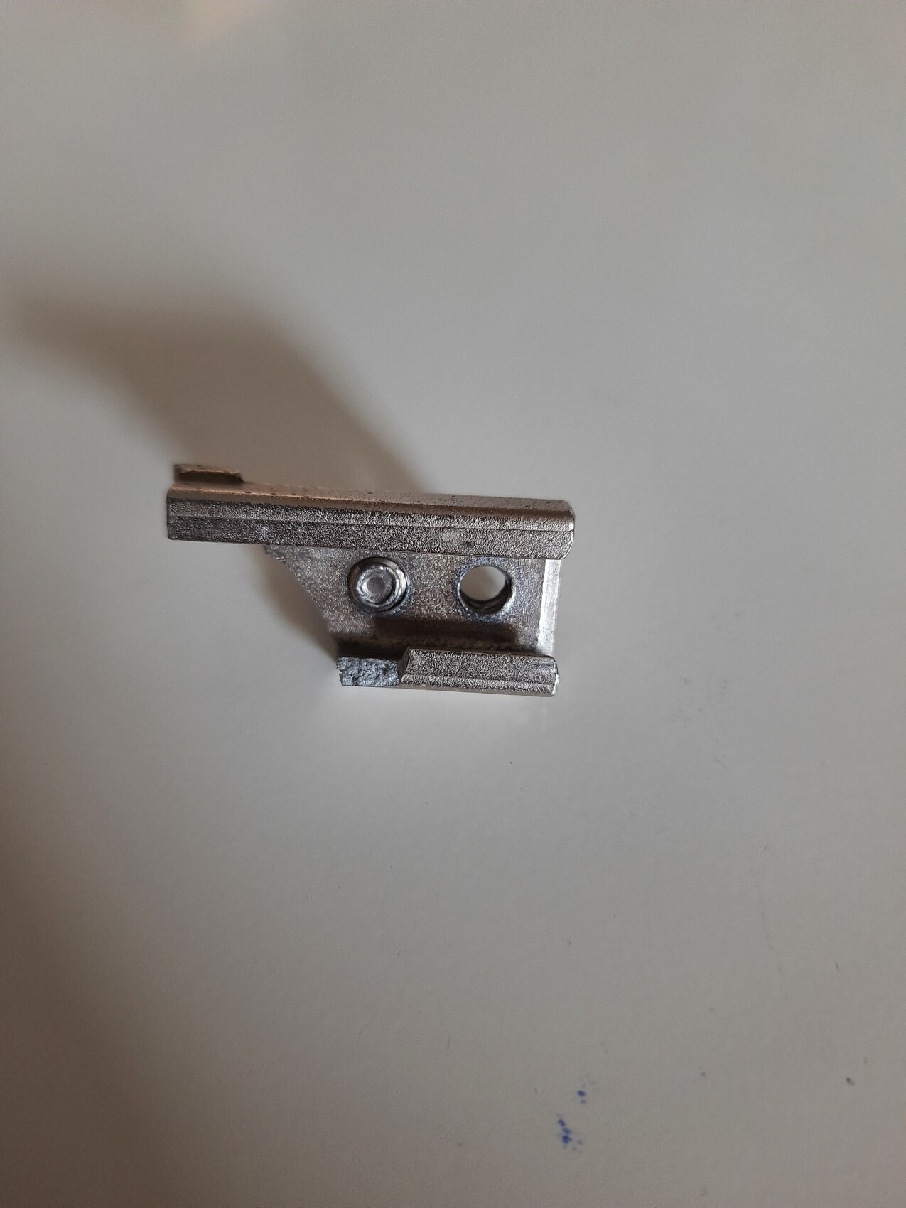 Kleine silberne Metallkomponente mit zwei Löchern und einer seitlichen Kante.