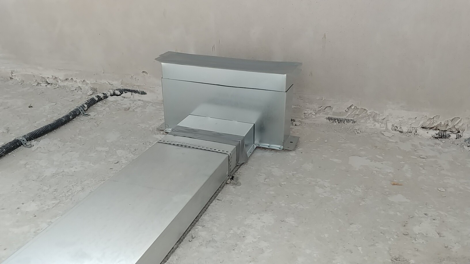 Metallischer Luftkanal im Baubereich, Installationskanal auf rohem Betonboden neben Wand