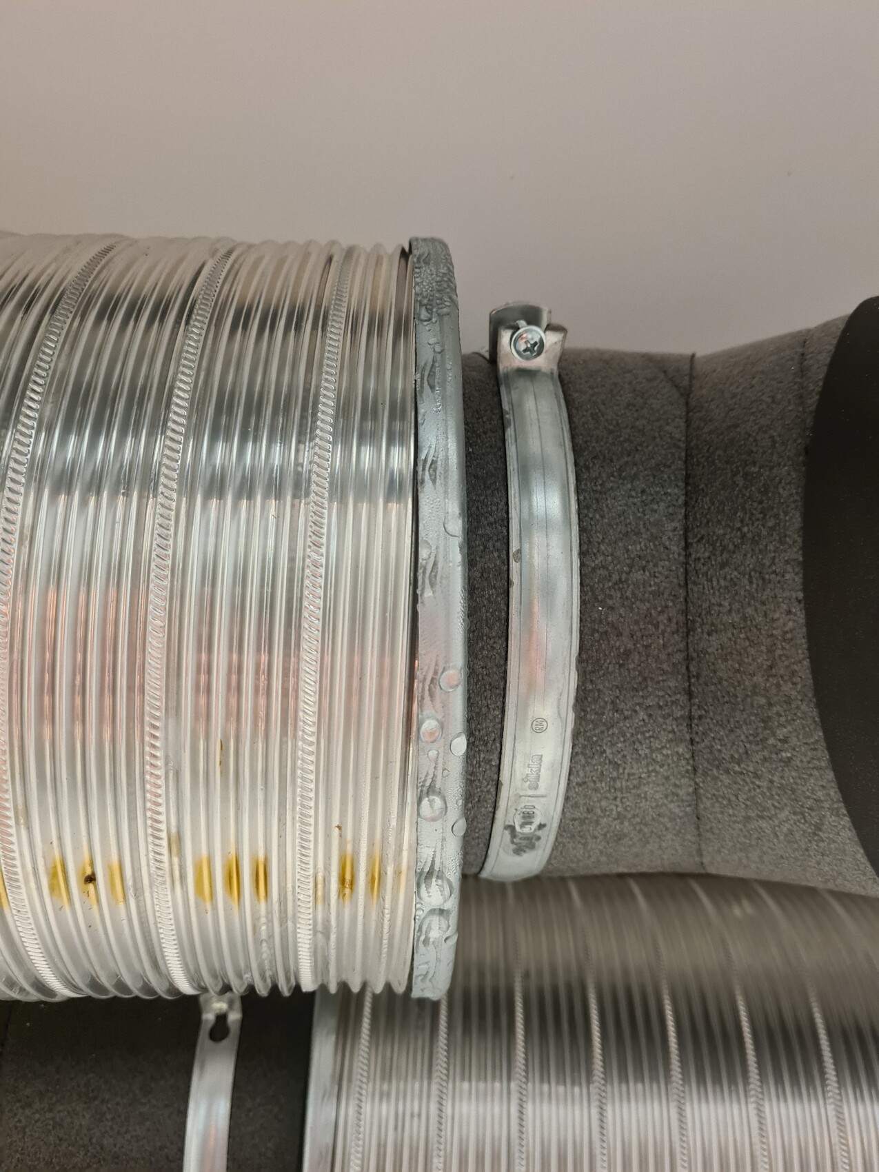 Spiralförmiger Metall-Lüftungsschlauch mit Klemmring und Dämmung, seitlich montiert.