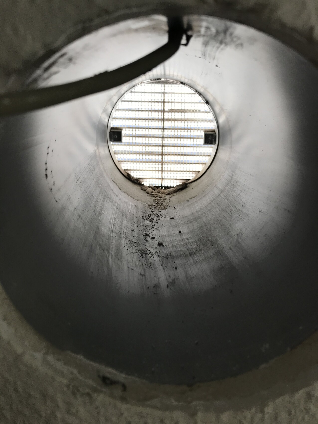 Blick durch ein rundes Metallrohr; am Ende eine Gitteröffnung lässt Licht hinein.