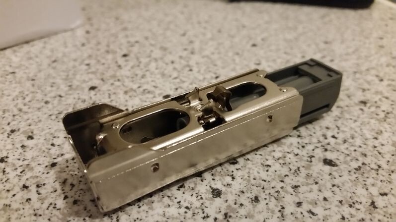 Metallisches, rechteckiges Bauteil mit zwei ovalen Öffnungen und schwarzem Endstück auf Steinplatte