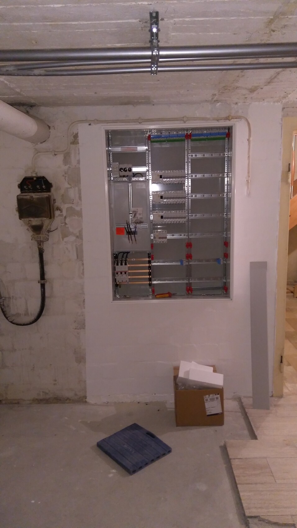 Verteilerschrank im Keller: Metallrahmen, Klemmenleisten, mehrere Kabelkanäle; Karton davor.
