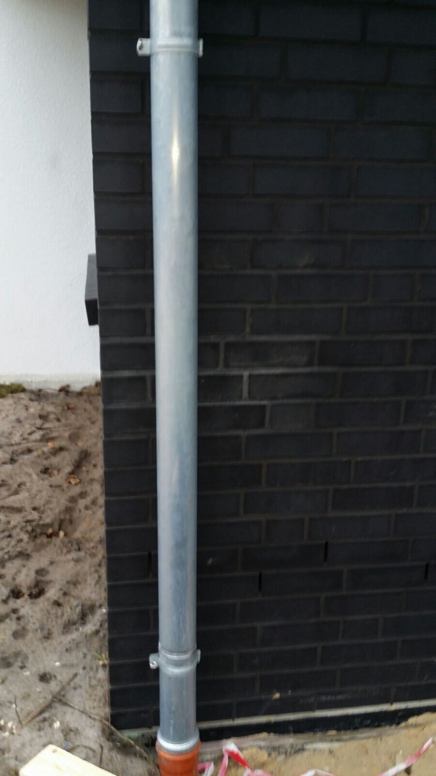 Metallisches Regenrohr montiert an dunkler Backsteinwand eines Hauses von außen.