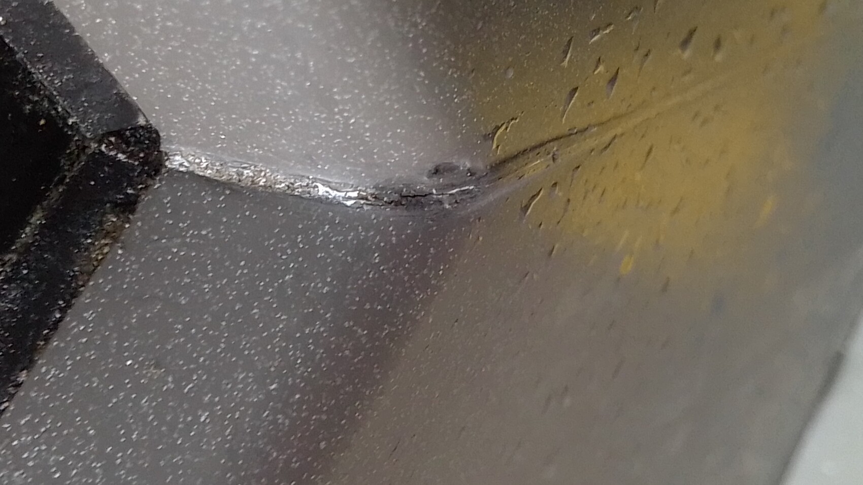 Nahaufnahme einer Metallkante mit Schweißnaht, staubige Oberfläche und gelb-braune Flecken.